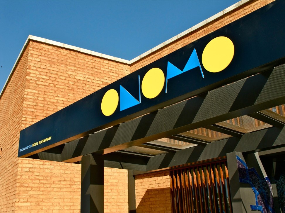 Onomo hotel entrance with yellow circles and blue triangles logo on dark signage against brick building.