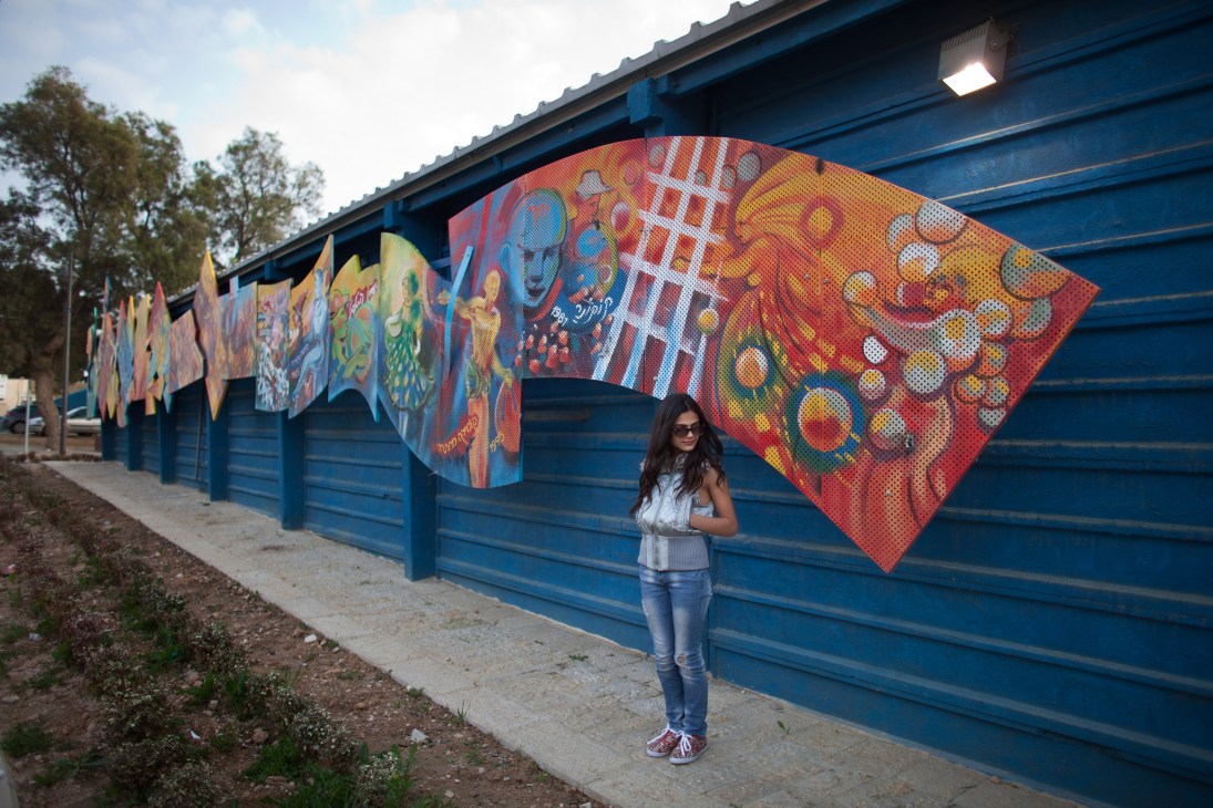 Woman posing for birthday photos in front of colorful street art mural on blue building