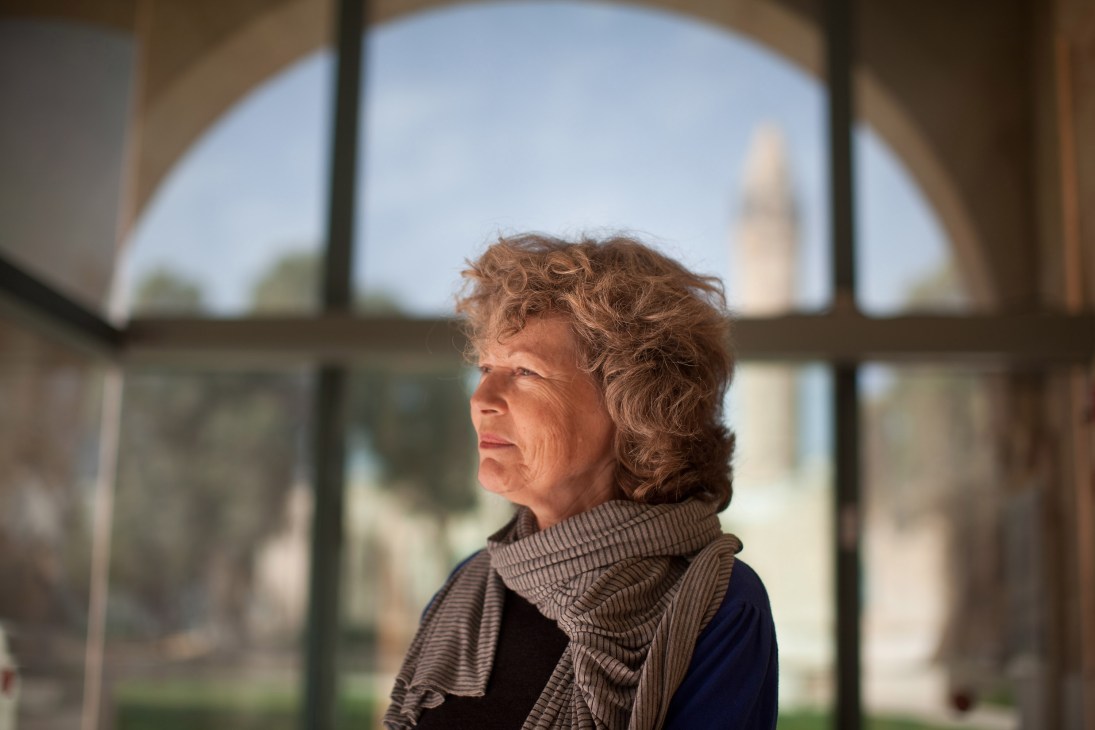 Woman with curly brown hair standing by arched window overlooking landscape
