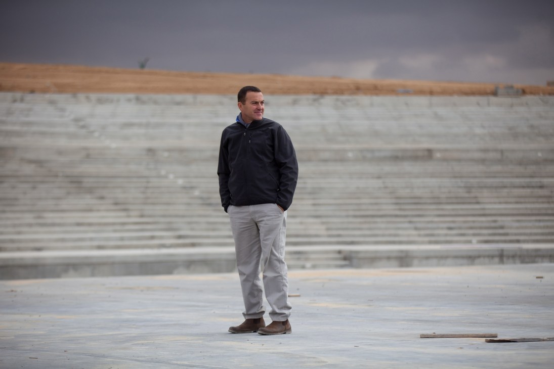 Man in black jacket and grey pants standing on concrete riverbed with water channels in background.
