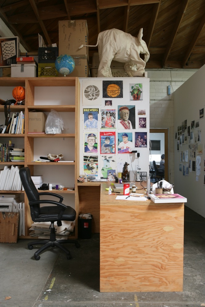 A painter's studio workspace with wooden shelving, desk, and mood board of portraits and images.