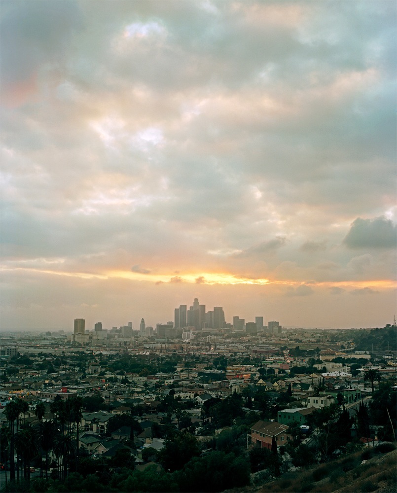 Los Angeles skyline with downtown buildings visible across sprawling residential neighborhoods at sunset.