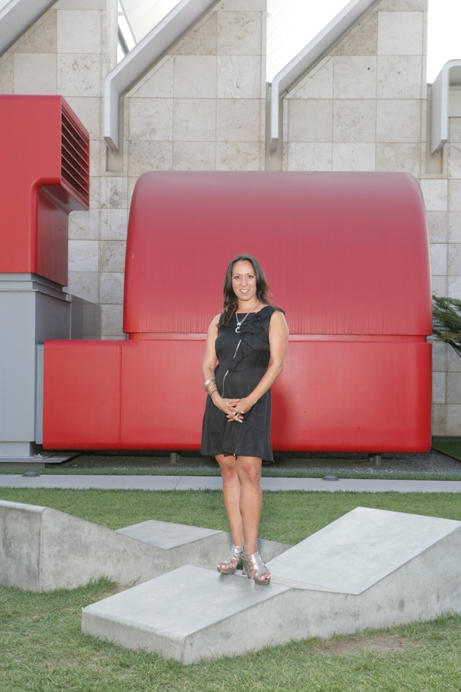 Shamim Momin, curator at LAND, stands in front of a large red sculptural installation at LACMA.