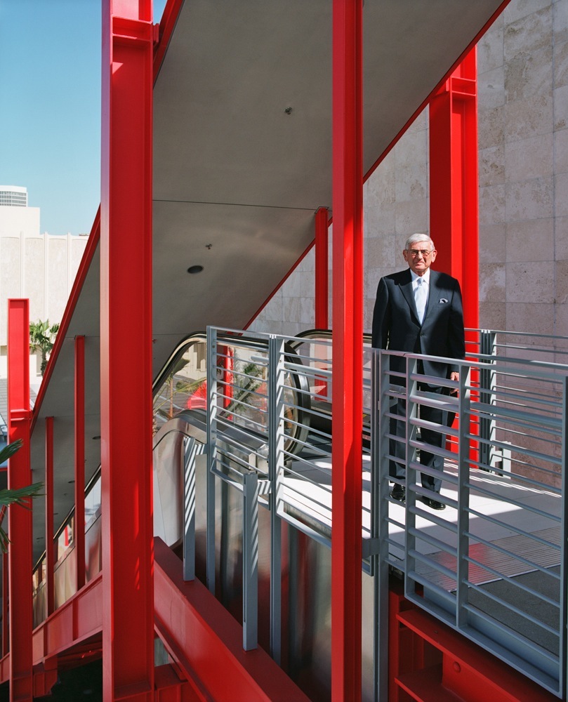 Eli Broad stands on a red metal staircase with modern architectural features.