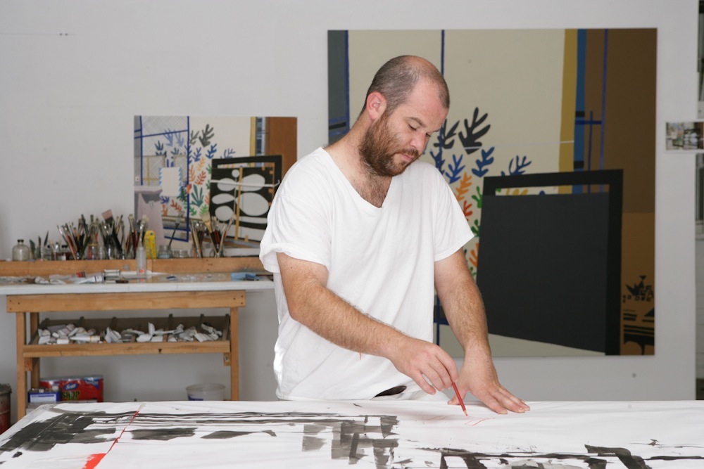 Painter Jonas Wood works on a canvas in his studio surrounded by art supplies and finished paintings.