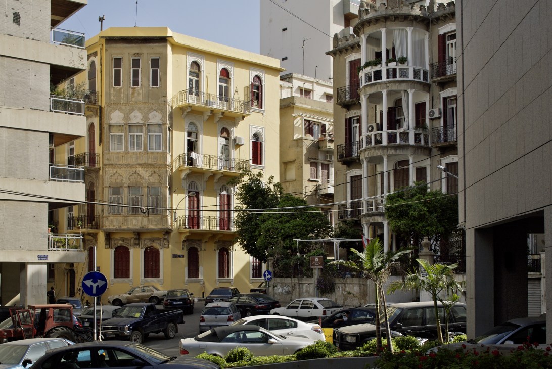 Historic yellow and cream-colored buildings with arched windows and ornate balconies in Ashrafieh's Furn el Hayek area, contrasted by modern concrete structures.