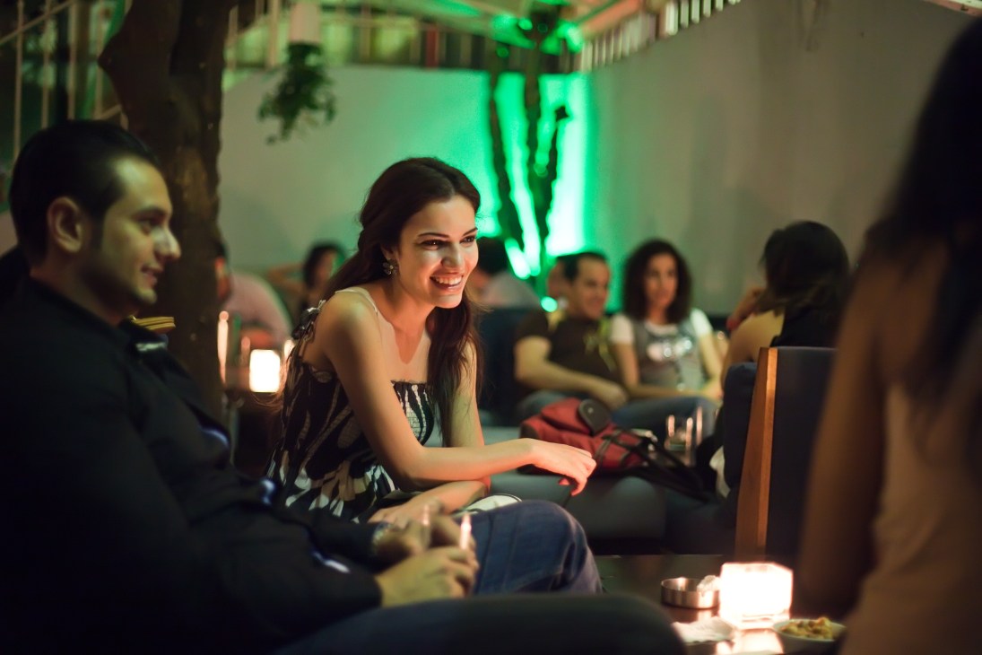People socializing at a bar with green neon lighting and candlelit tables at night