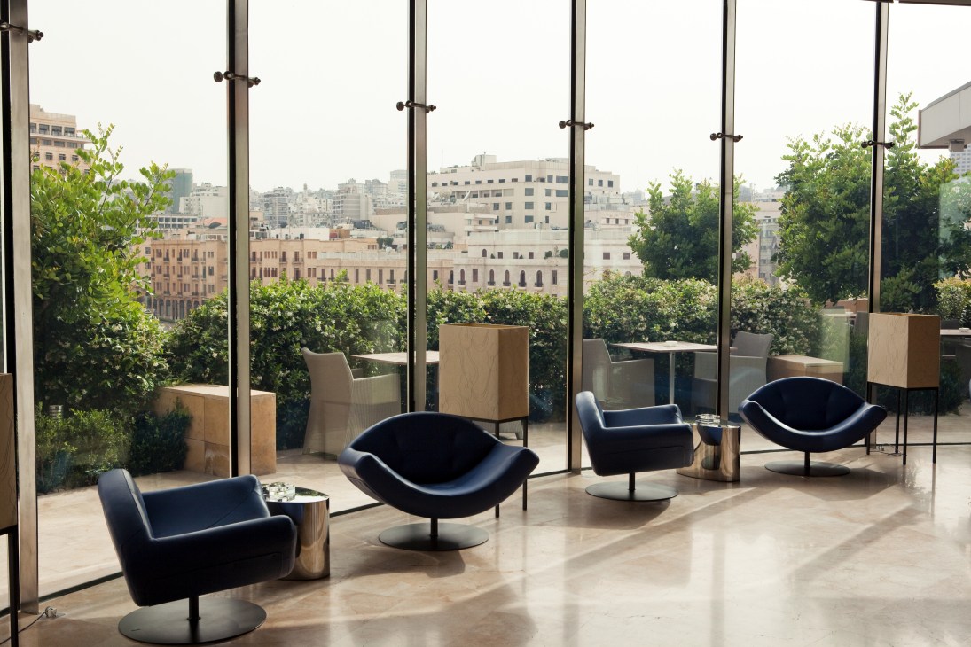 Modern lounge with black chairs overlooking Beirut cityscape through floor-to-ceiling windows at Le Gray hotel.