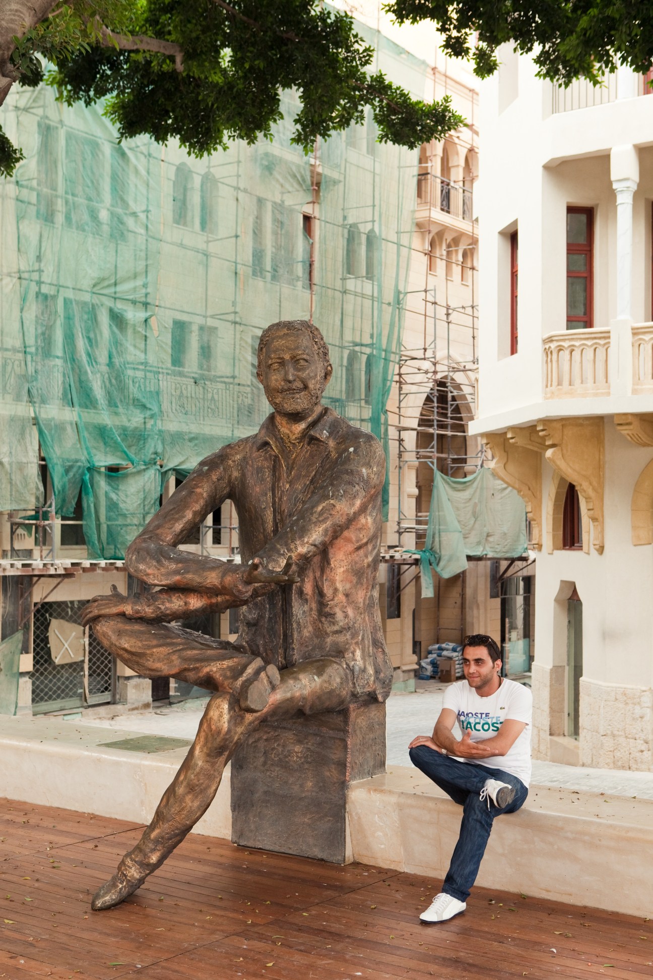 Man sitting next to bronze statue of journalist Samir Kassir in Beirut courtyard under construction.