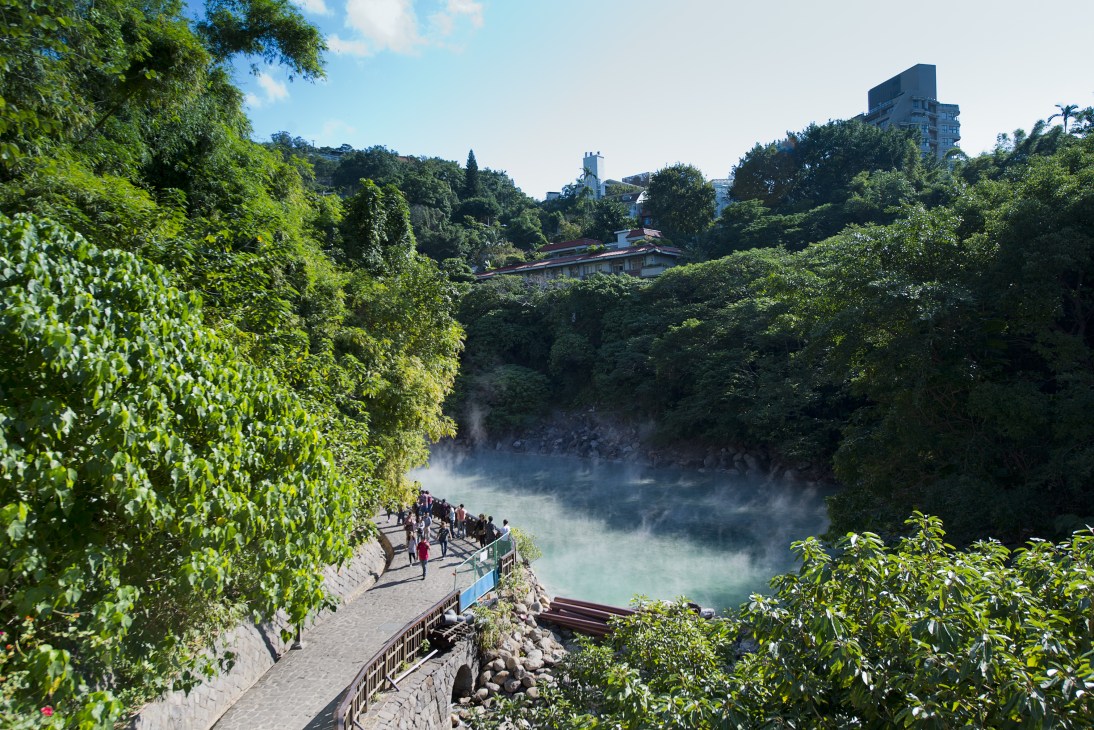 Beitou's thermal valley with steaming hot springs surrounded by lush green mountains and visitors on viewing platform.