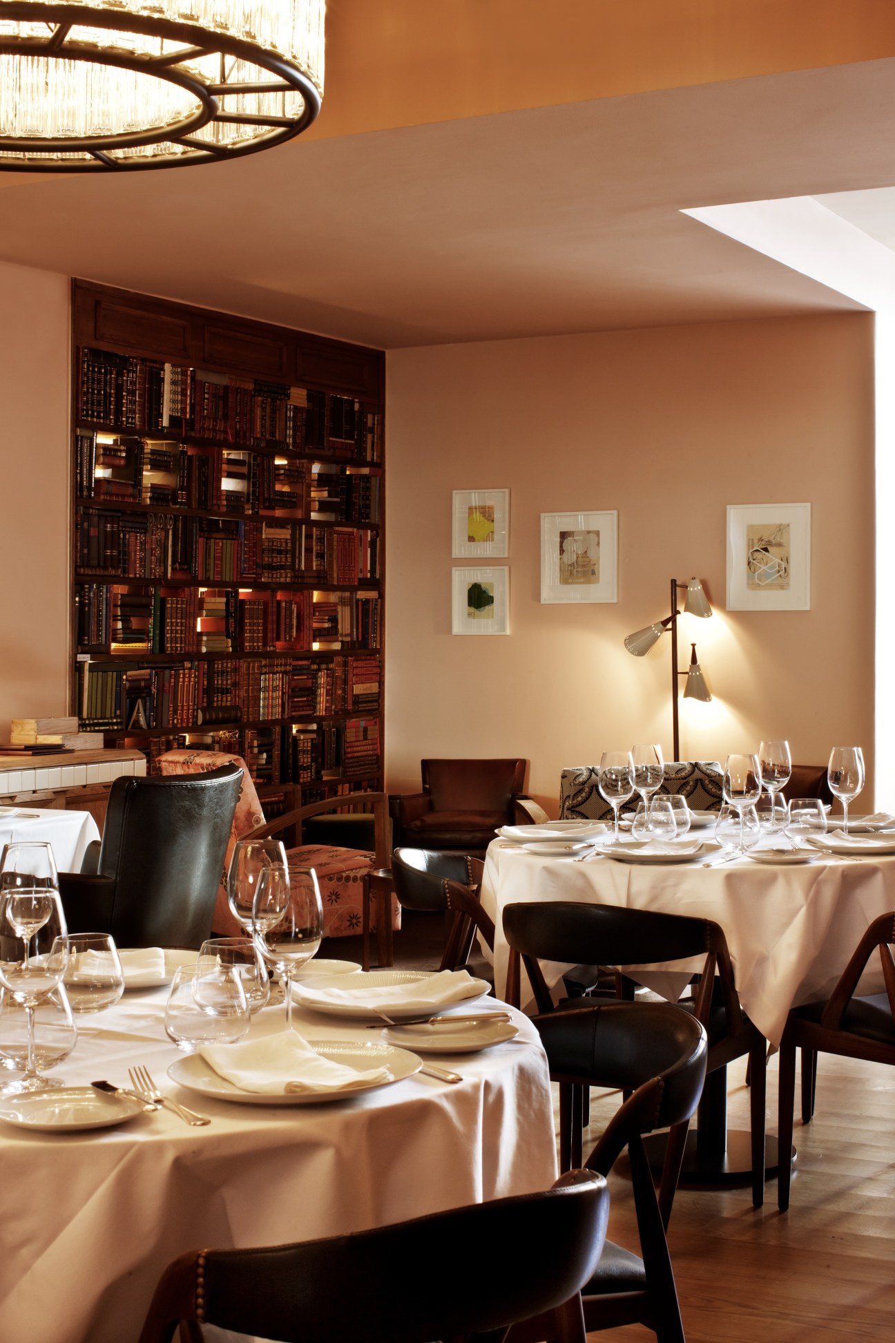Fine dining room at Belcanto with set tables, floor-to-ceiling bookshelf, and modern pendant lighting.