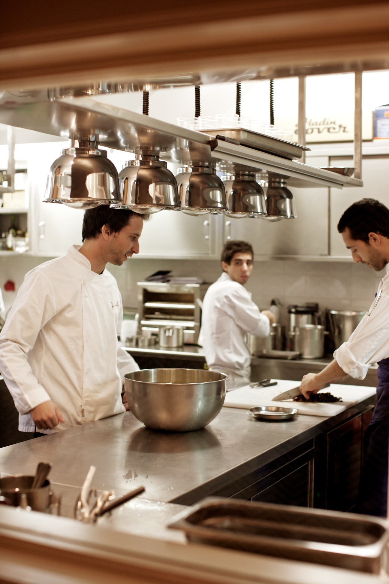 Chefs in white uniforms work in Belcanto's kitchen with stainless steel pendant lights and equipment.
