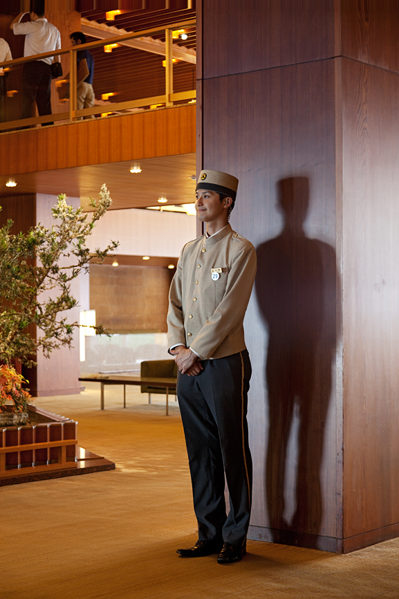 Bellboy in uniform standing in the modernist lobby of Hotel Okura's main wing.