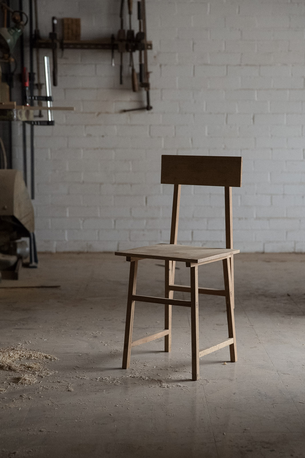 Wooden chair with simple joinery displayed in a workshop with white brick walls.