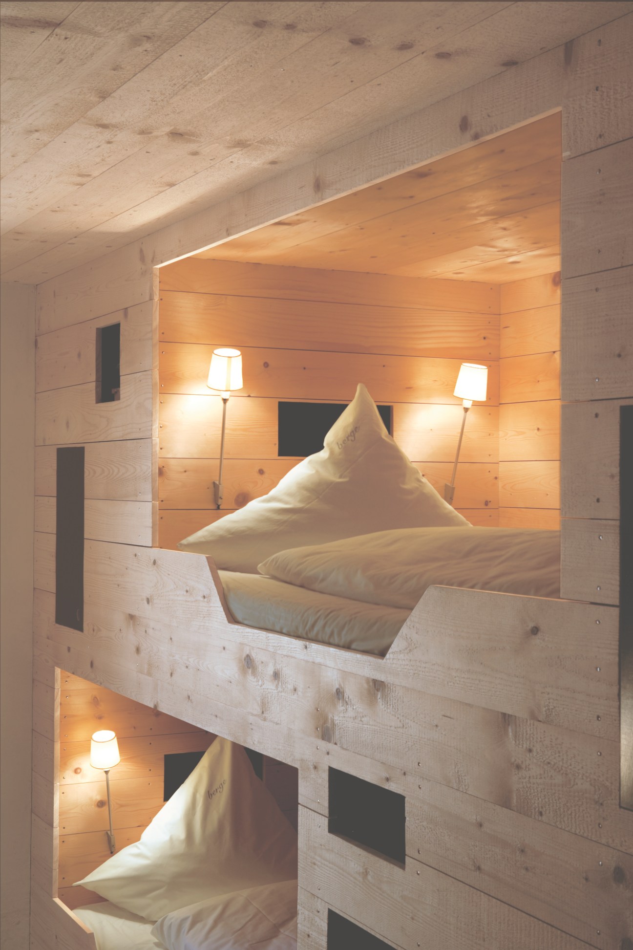 Interior of a Berge apartment showing stacked wooden bunk beds with white pillows and ambient lighting.