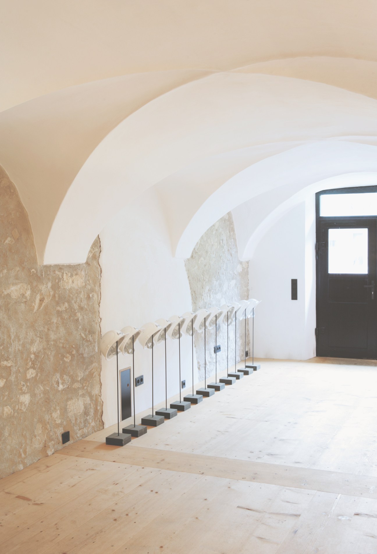 Interior of Berge apartment showing Alpine spruce flooring, arched white ceiling, stone wall, steel door knobs, and modern furnishings.