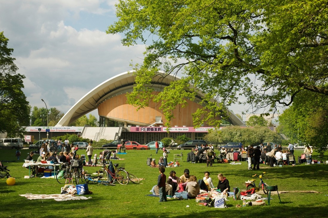 People picnicking on a grass field with the Haus der Kulturen der Welt building in the background.