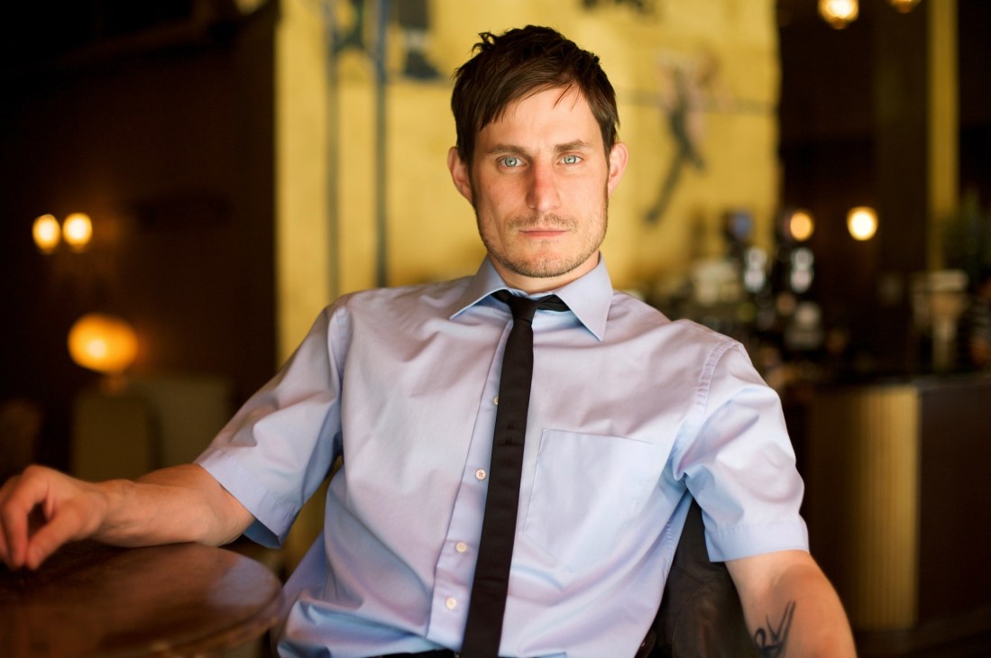 Actor Clemens Schick in a light blue shirt and dark tie, photographed indoors with warm lighting.