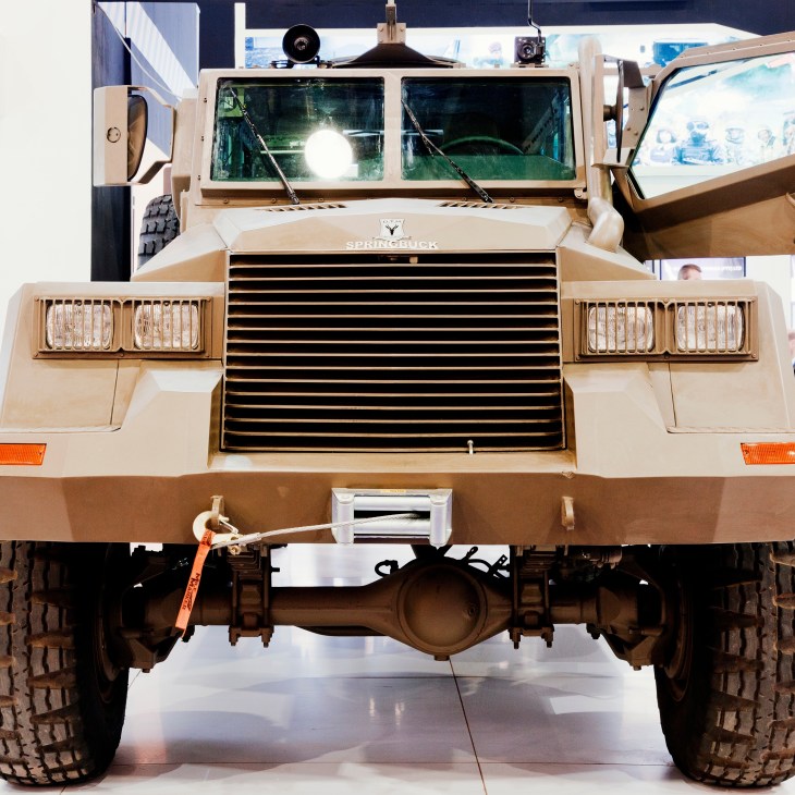 Front view of the South African Springbuck armoured vehicle displaying its tan-colored plating, reinforced headlights, and grille.
