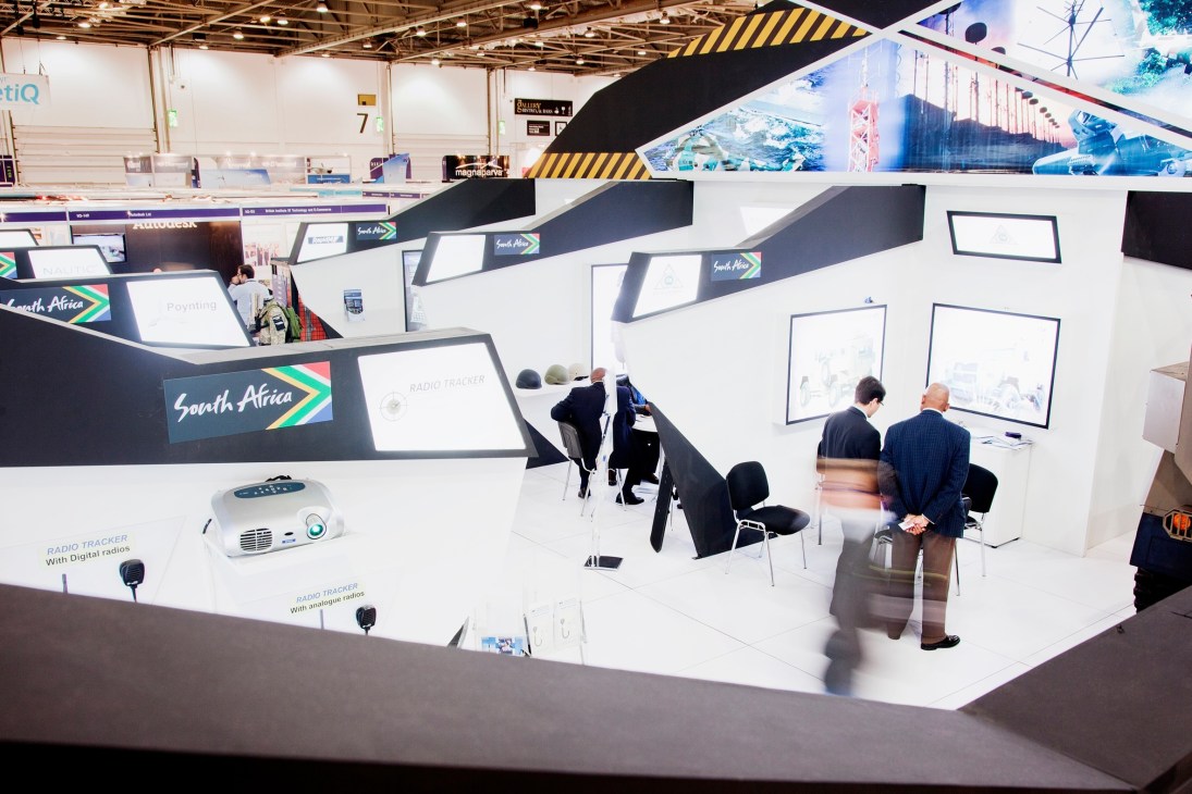 South Africa Pavilion at DSEi defence exhibition featuring white and black modern booth design with country branding and display screens.