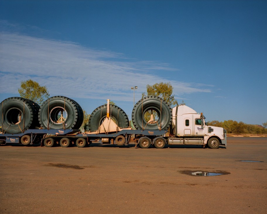 A large truck carrying oversized industrial tires parked in the Australian outback under a clear blue sky.