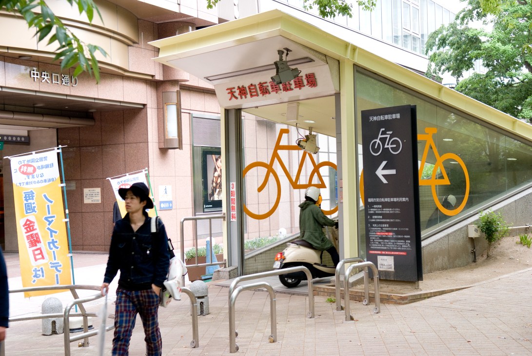 Underground bike parking facility near Tenjin station with orange bicycle symbols and signage in Japanese.