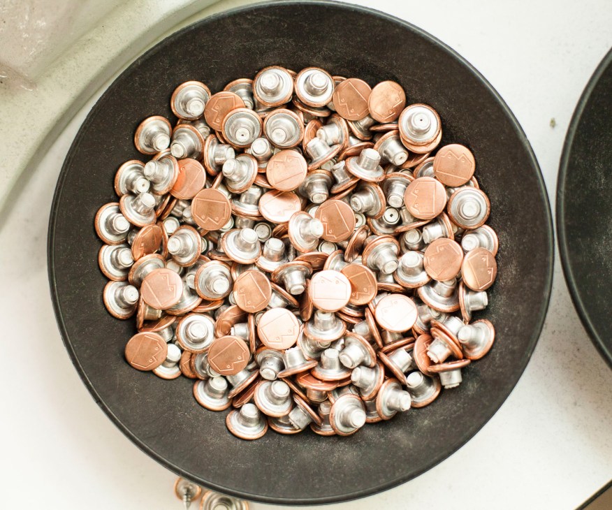 Metal buttons and copper-colored fasteners arranged in a dark bowl.