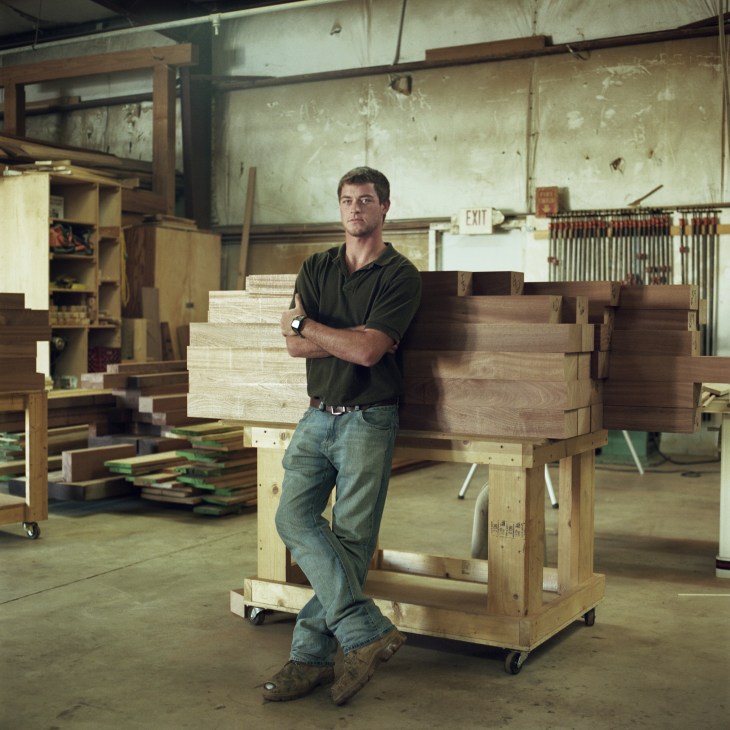 Peter McGinnis, a carpentry student, stands with arms crossed in a workshop surrounded by wooden beams and materials.