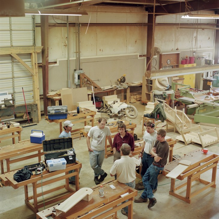Professor Ken Nuttle teaches a woodworking class to students in a workshop space filled with wooden furniture projects and tools.