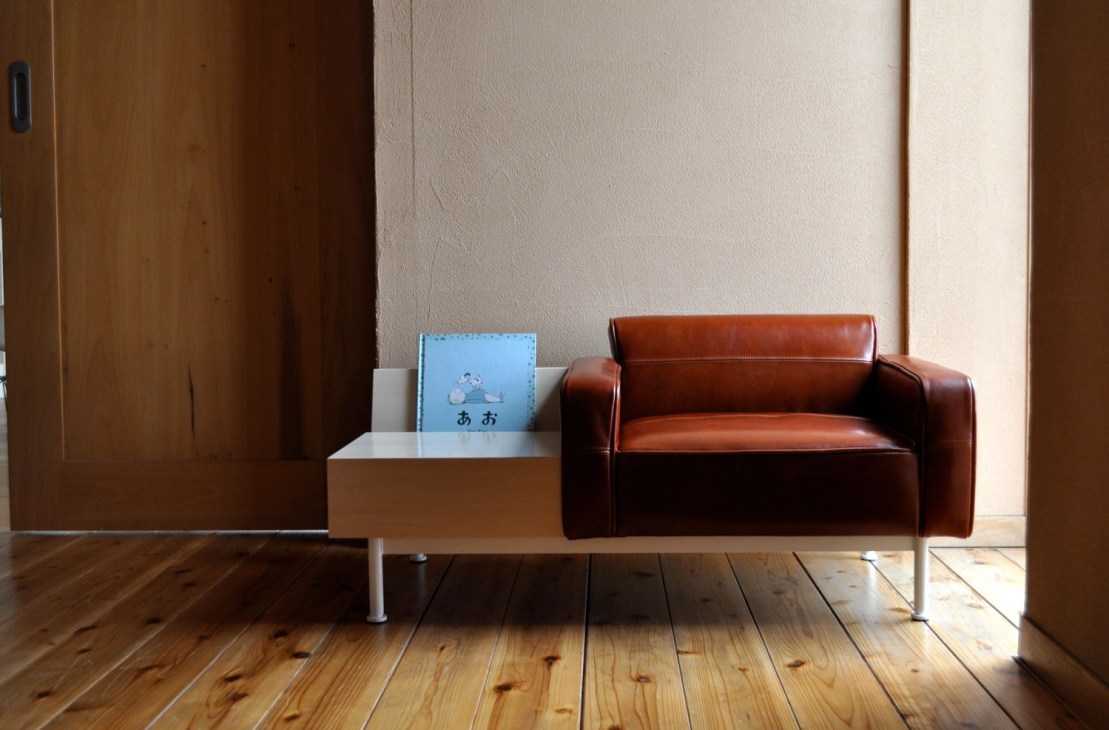 Blue Quince children's furniture including a white storage bench and cognac leather sofa in a minimalist room.