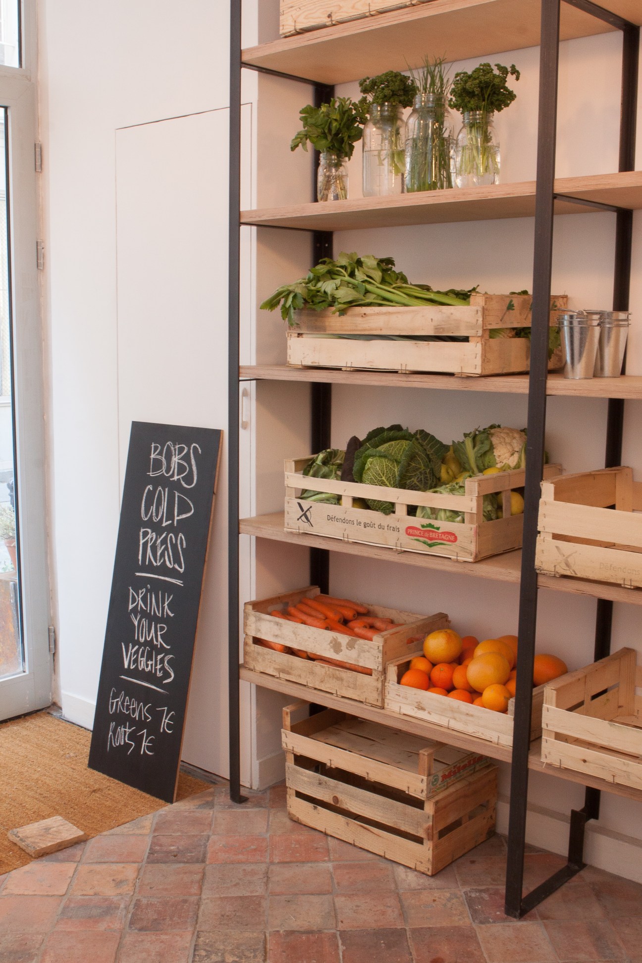 Bob's Cold Press juice shop interior with wooden shelving displaying fresh produce and flowers in glass vases.