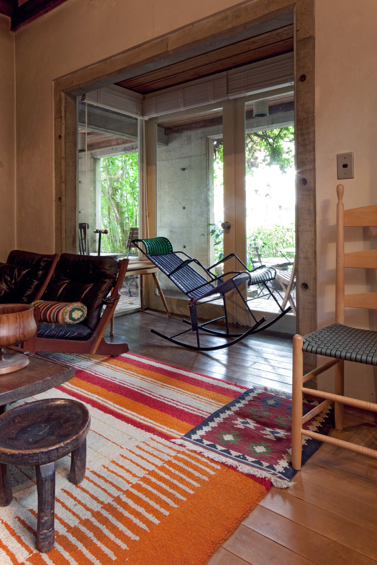 Living room interior with woven rocking chair, colorful striped rugs, and view to garden terrace