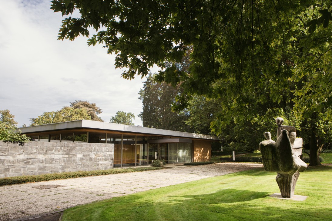 Kanzlerbungalow, a modernist single-story building with stone walls and wide overhanging roof, set in manicured grounds with sculpture.