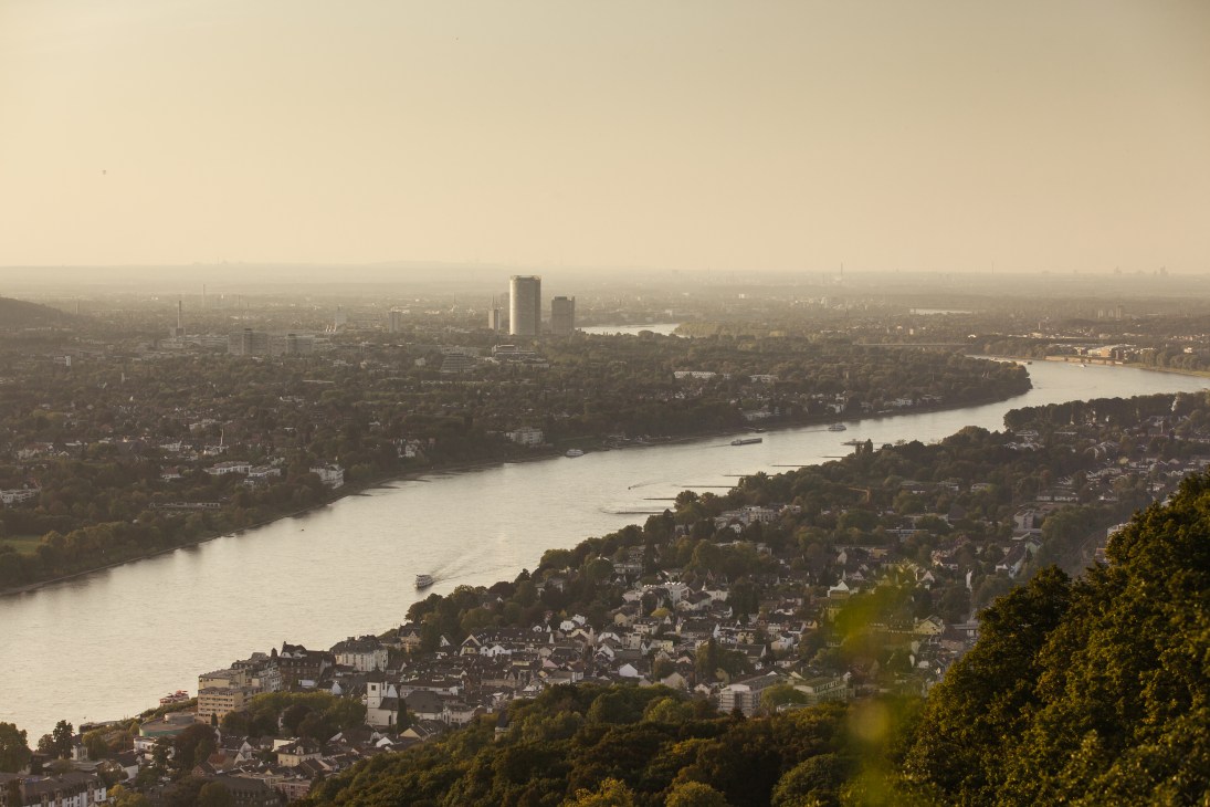 Aerial view of Bonn with the Rhine River winding through the city and forested hills beyond.