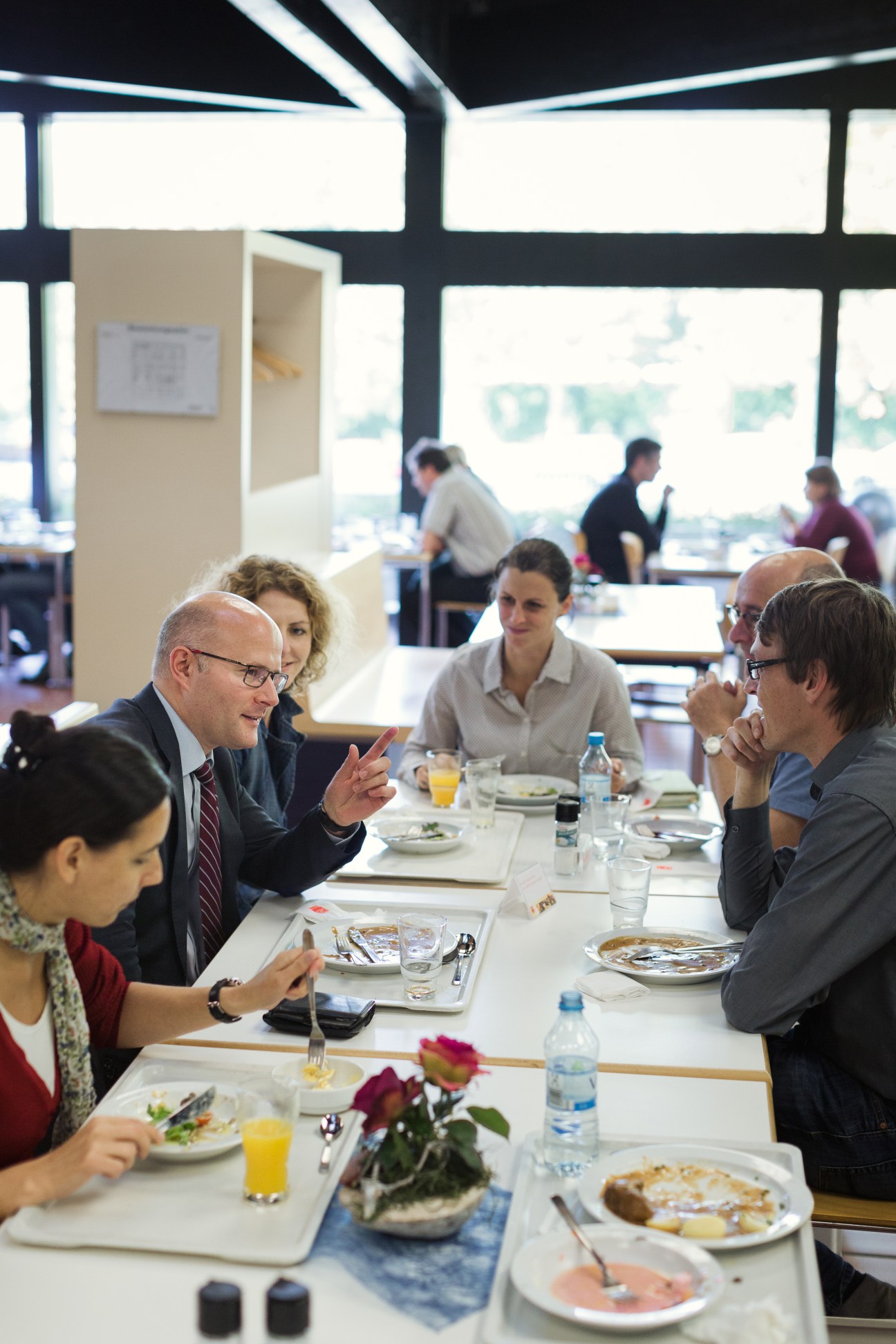 Michael Vorländer dines with colleagues at a table in a bright cafeteria with views overlooking the Rhine.