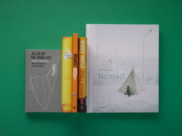 Five books displayed against a green background including Atlas of the Conflict, The Tiger's Wife, and Nomad by Jeroen Toirkens.