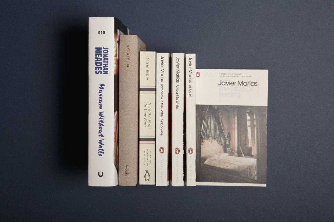 Collection of books arranged by spine, including works by Javier Marías and other literature displayed against a dark background.