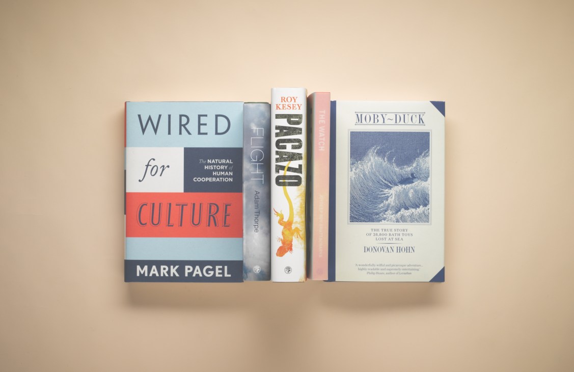 Five books displayed on a beige shelf including Wired for Culture by Mark Pagel, Flight by Adam Thorpe, Pacazo by Roy Kesey, and Moby-Duck by Donovan Hohn.