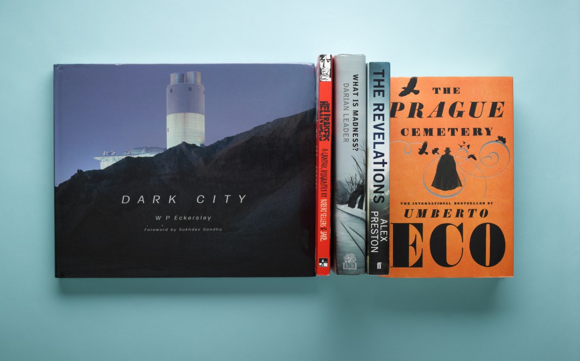 Four books arranged horizontally on a light blue surface, including Dark City by W.P. Eckersley and The Prague Cemetery by Umberto Eco.