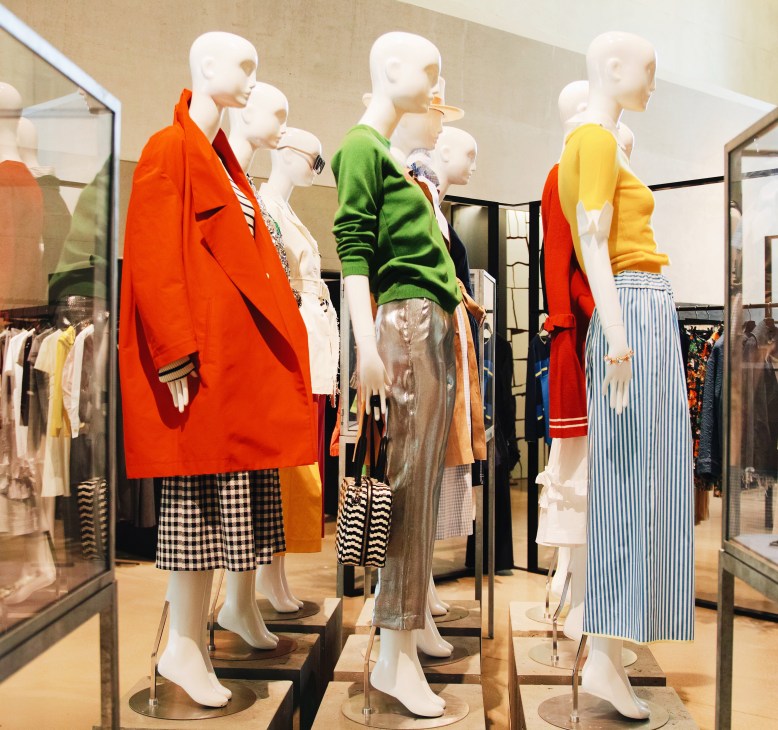 Fashion mannequins dressed in colorful outfits including red blazers, green sweaters, and yellow tops displayed in a modern retail space.