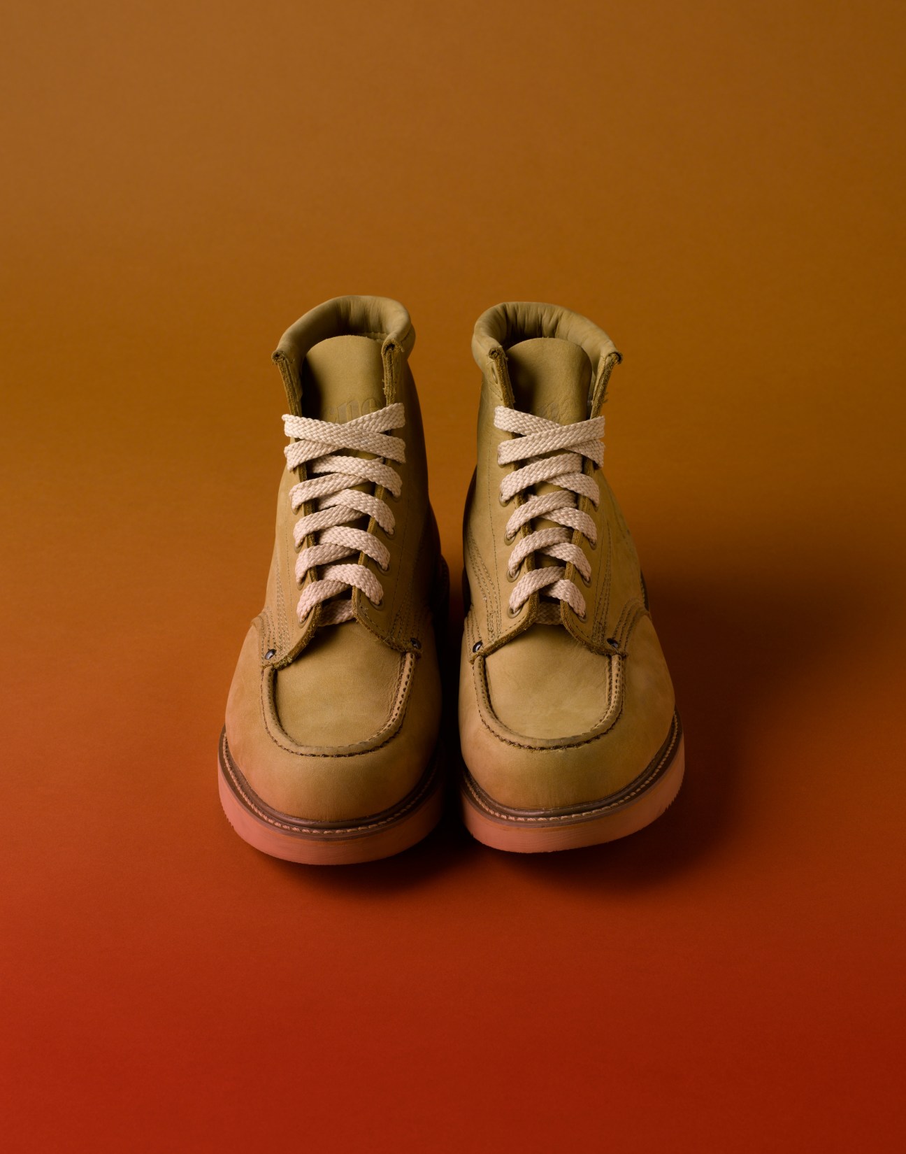 Pair of sand-colored leather workman's boots with cream laces and oil-resistant soles against an orange background.
