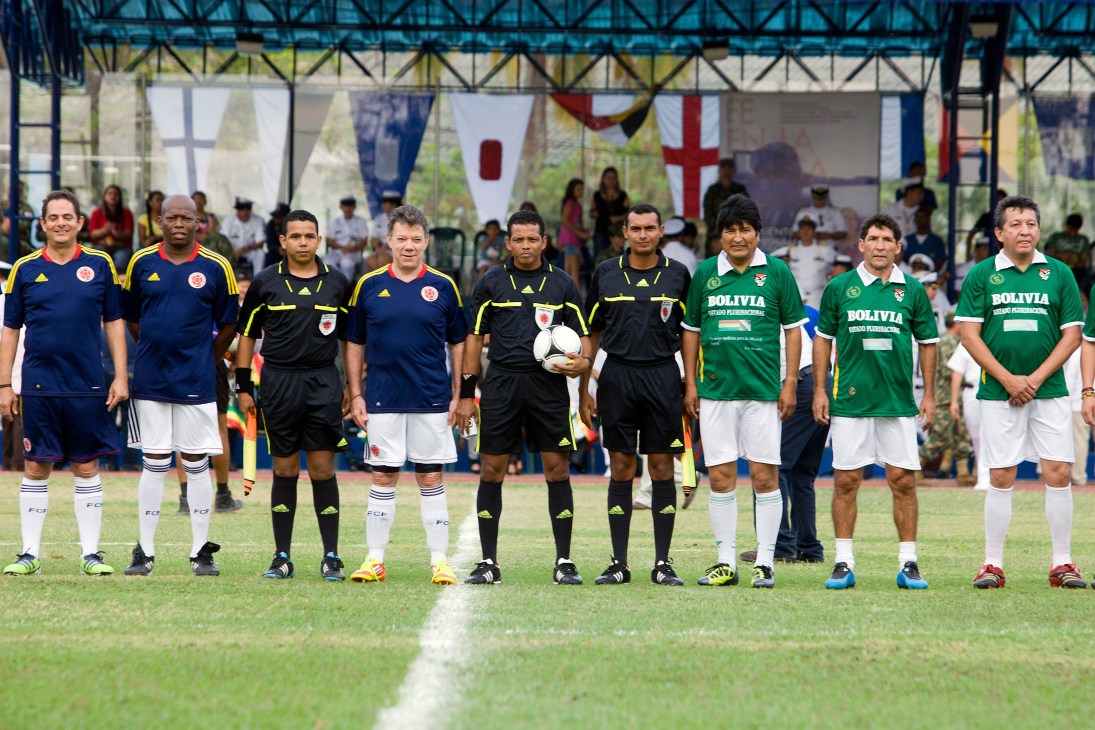 Football teams from Colombia and Bolivia line up on a grass field before a match at the Summit of the Americas.