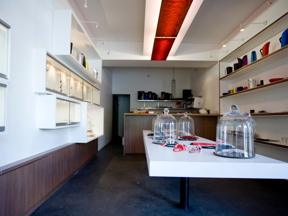 Modern minimalist retail interior with white display counter, wooden shelving, and red ceiling accent lighting.