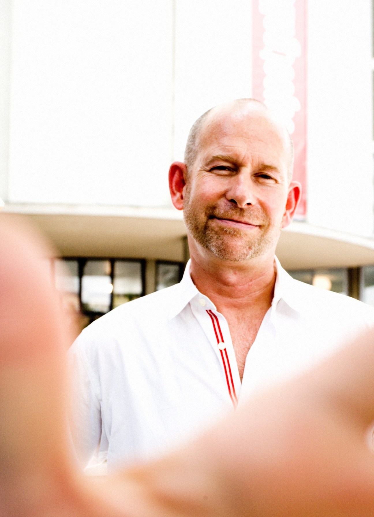 Portrait of a man in a white shirt with red accents standing in front of a modern building.