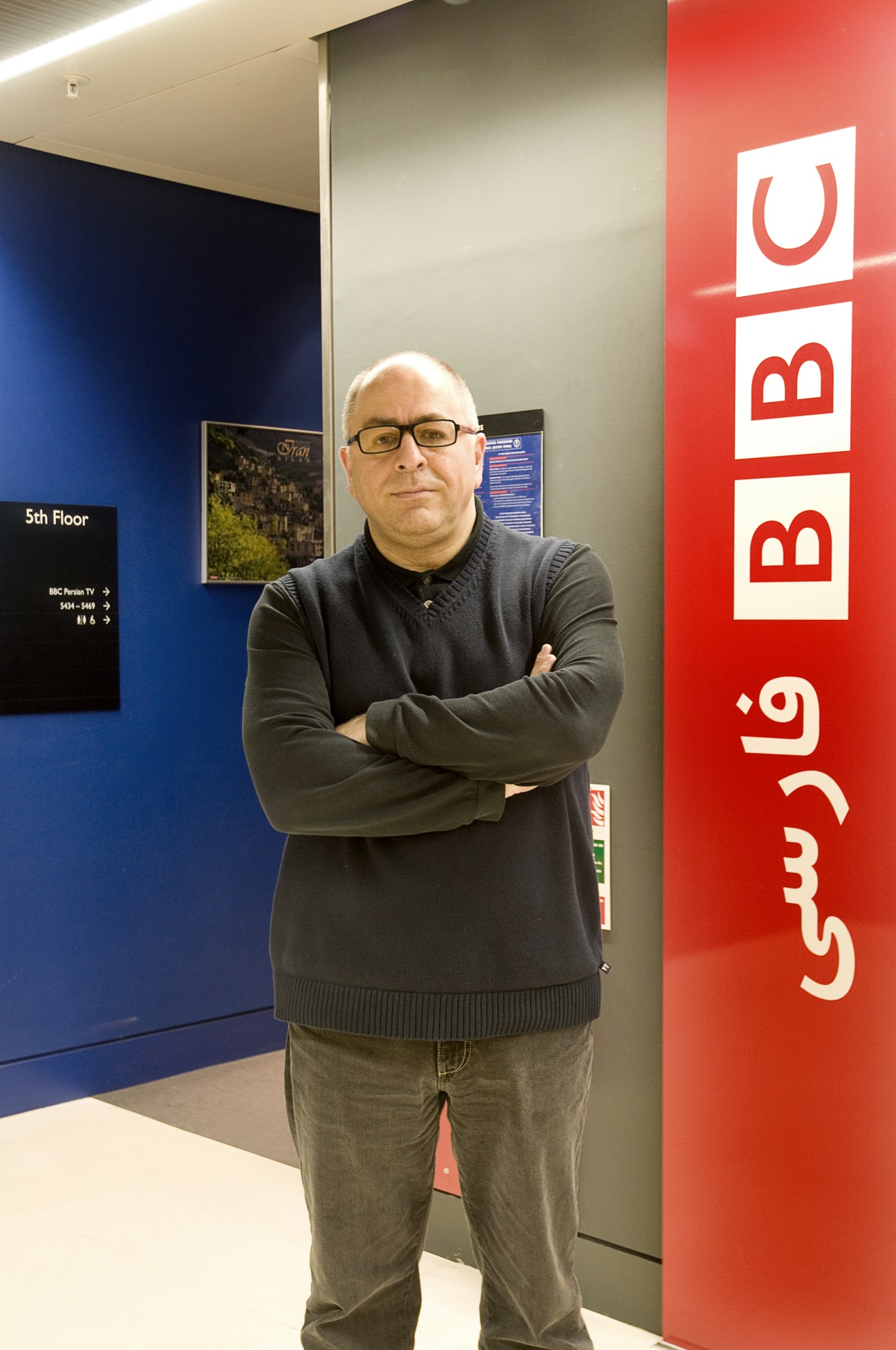 Man standing in hallway next to BBC Persian TV signage at Broadcasting House.