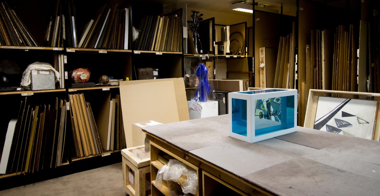 Sotheby's storage area with shelving, framed artworks, and a display dummy for Damien Hirst auction.