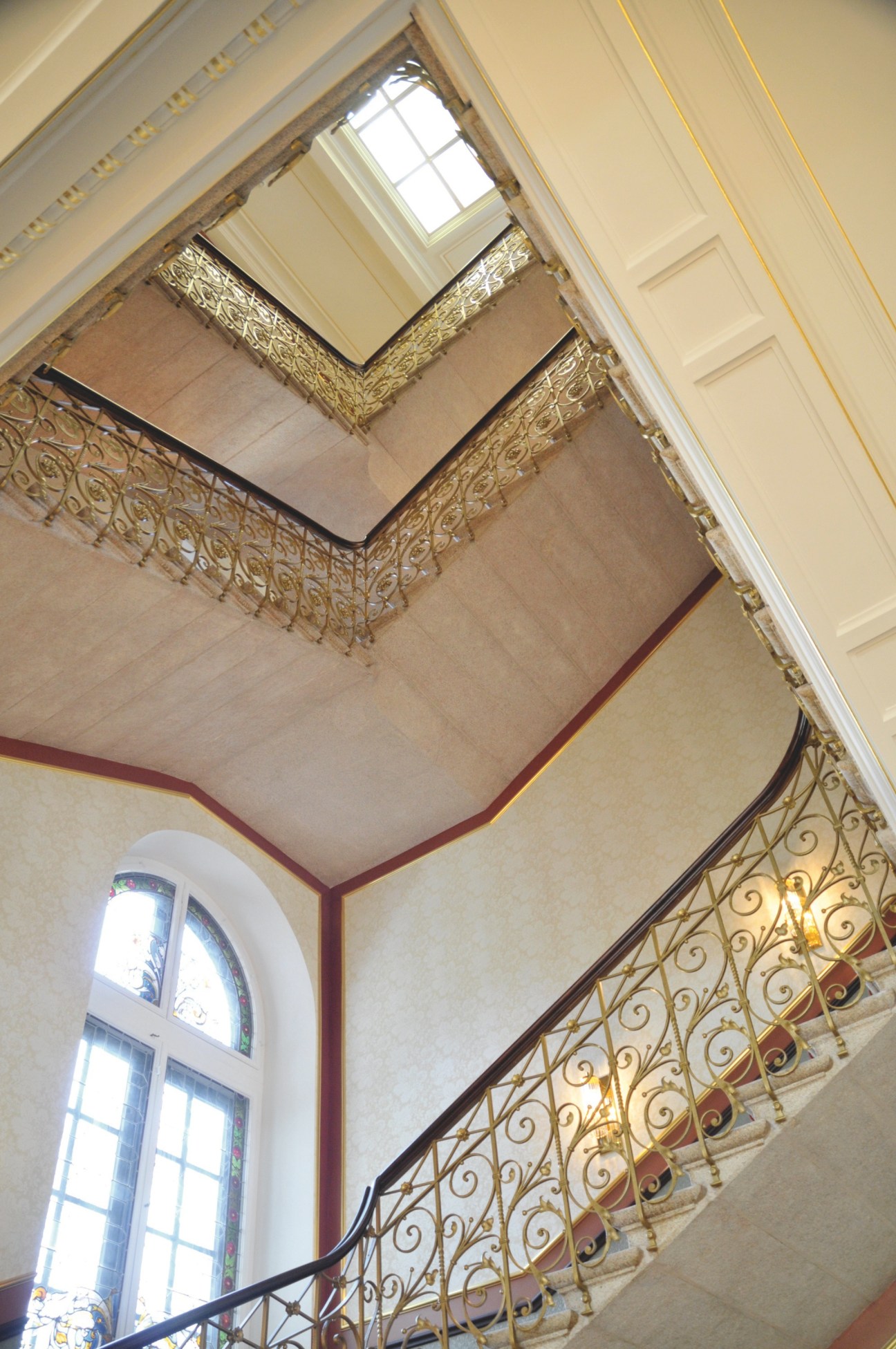 The original staircase at Dolder Grand hotel, viewed from the main lobby, showing ornate gold railings and skylight.