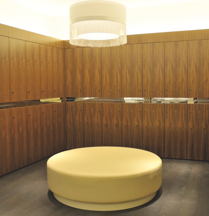 Minimalist changing room with wood-paneled walls, circular yellow ottoman seating, and modern ceiling light.