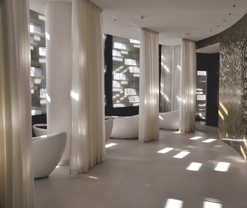 Modern spa treatment room with white soaking tubs separated by cream curtains and Japanese hot stone relaxation beds.