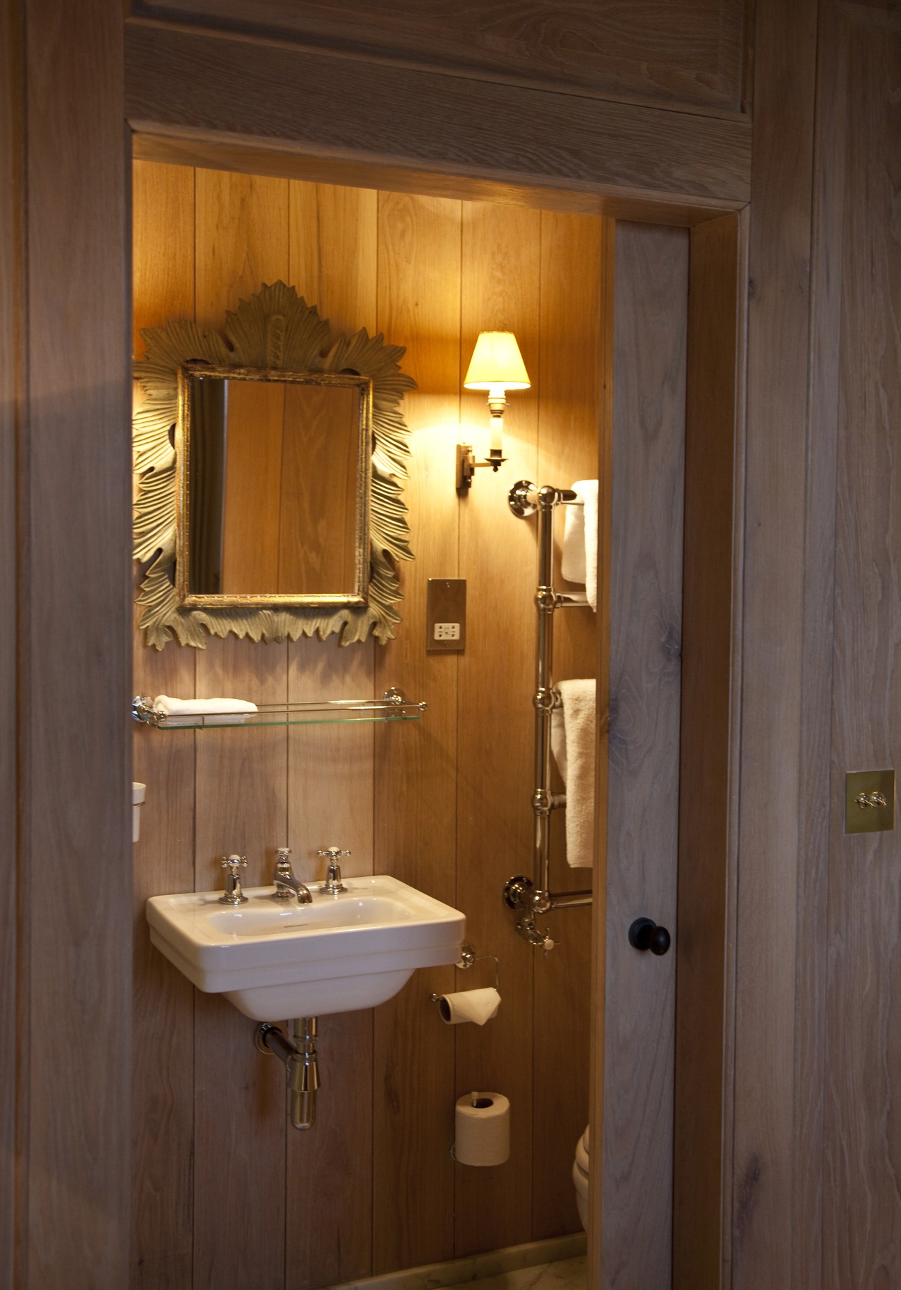 Wooden bathroom interior with sink, ornate mirror, wall sconce, and shower fixtures at The Orange hotel in London.
